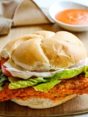 Buffalo Chicken Sandwich on cutting board with buffalo sauce in background