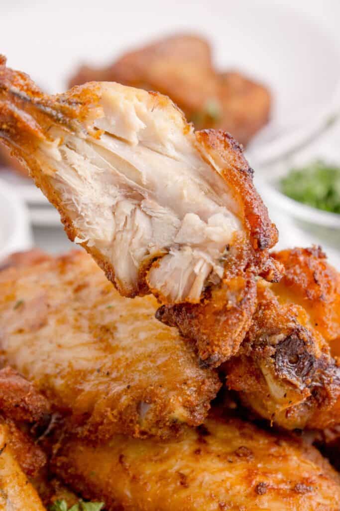 Close up of air fried chicken wing being held with a bite taken out of it.