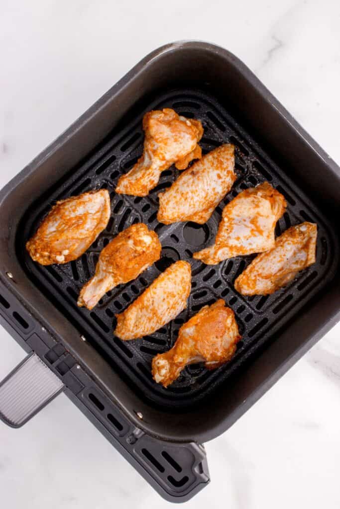 Raw chicken wings in an air fryer basket.