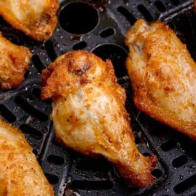 Close-up of cooked air fryer wings in an air fryer basket.