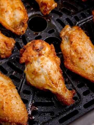 Close-up of cooked air fryer wings in an air fryer basket.