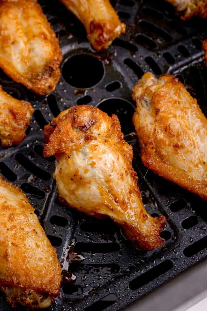 Close-up of cooked air fryer wings in an air fryer basket.