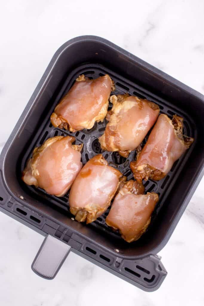 Raw marinated chicken thighs in an air fryer basket.