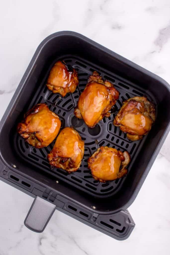 Cooked marinated chicken thighs in an air fryer basket.