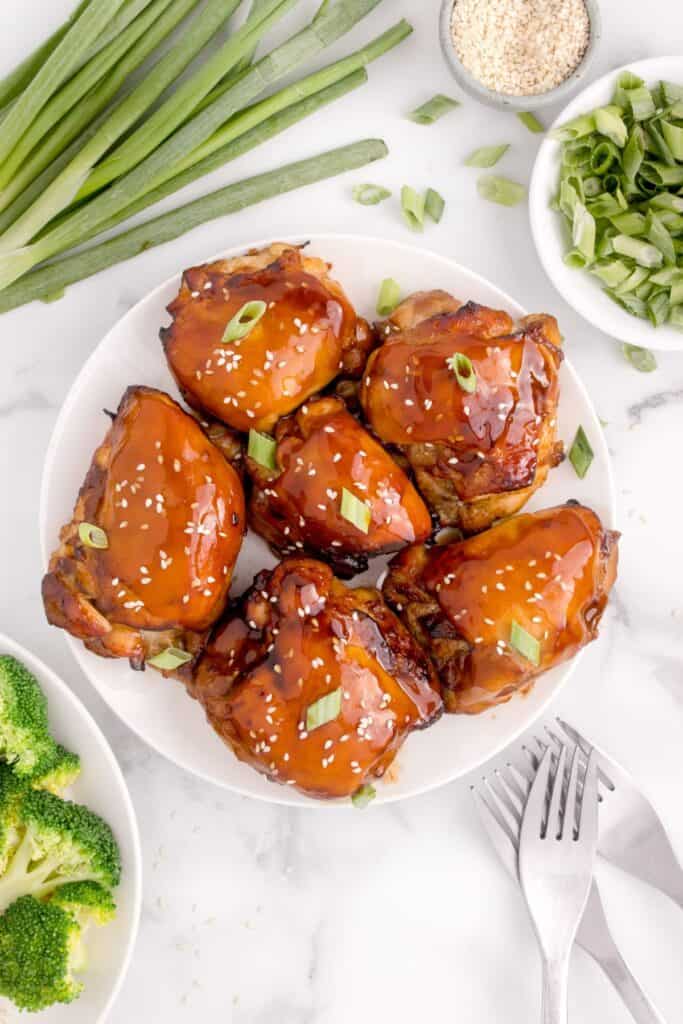 Air fry chicken thighs sitting on a white plate with extra marinade glazed on top.