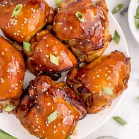 Close up of air fried chicken thighs sitting on a white plate with extra marinade glazed on top.