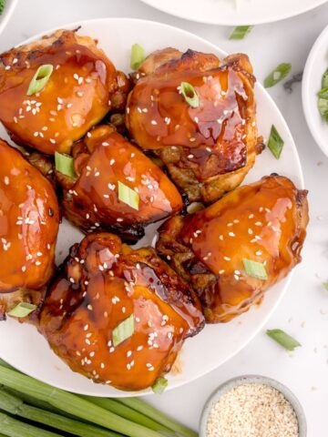 Close up of air fried chicken thighs sitting on a white plate with extra marinade glazed on top.