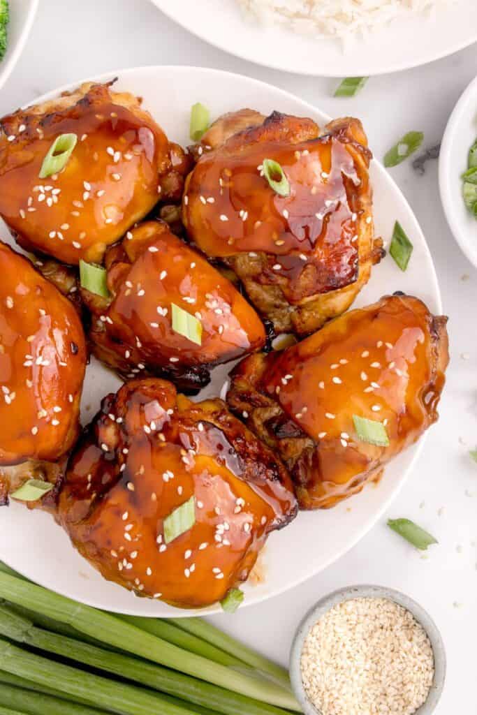 Close up of air fried chicken thighs sitting on a white plate with extra marinade glazed on top.