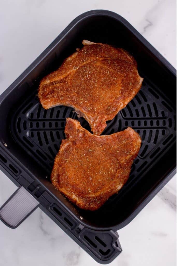 Raw pork chops in an air fryer basket from over top.