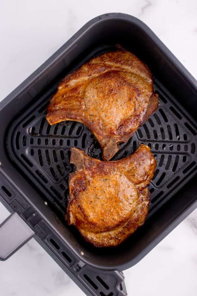 Cooked pork chops in the air fryer basket from over top.