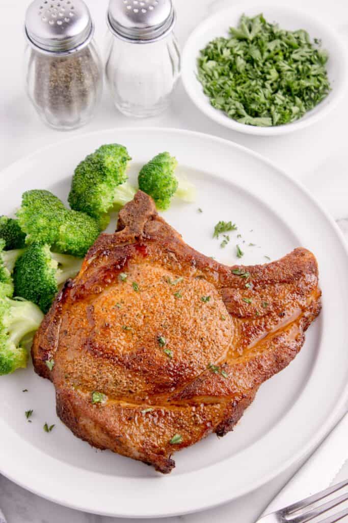 Cooked air fry pork chop on a plate with broccoli next to it.