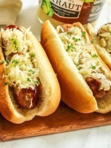 Air Fryer Brats in buns with sauerkraut on top and hand grabbing one