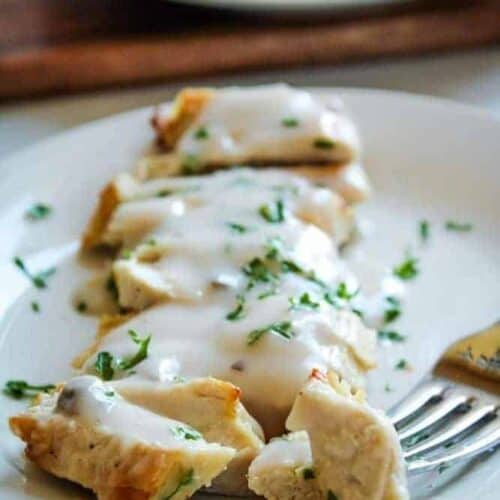 Air Fryer Turkey Cutlets covered in mushroom sauce sliced on a white plate with a fork in one piece