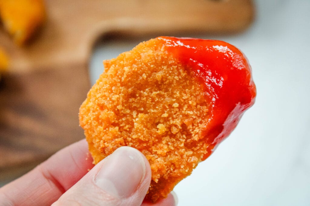Closeup of air fryer chicken nugget in hand with ketchup on it