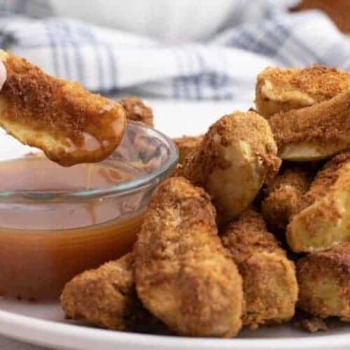 Air fryer apples on a white plate with one wedge being dipped in caramel