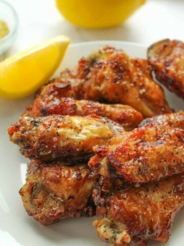 Lemon Pepper Air Fryer Wings on a white plate with a lemon slice and full lemon in the background