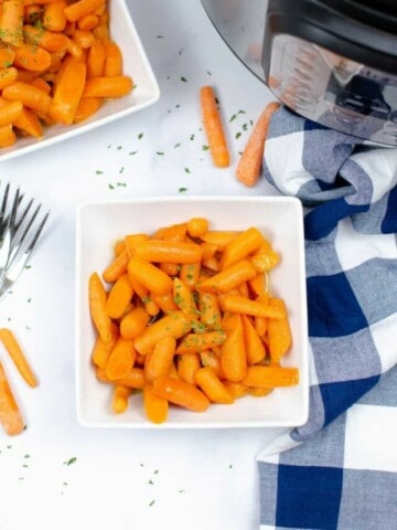 Glazed carrots in a white square bowl with white and blue checkered tablecloth and Instant Pot next to it