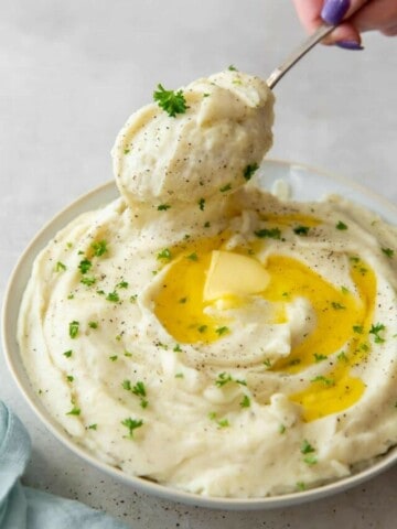 Instant Pot Garlic Mashed Poateos in a bowl with butter melting in it and spoonful of mashed potatoes being taken out