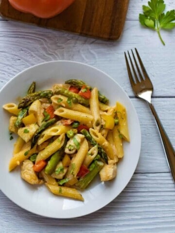 Chicken Chipotle Pasta on a white plate with a fork and orange pepper in the background