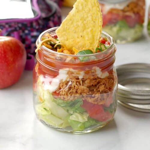 Chicken taco salad inside a mason jar with a tortilla chip sticking out of the top.