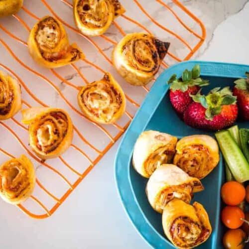 Pizza roll ups on a wired rack next to them served on a plate with fruits and vegetables.