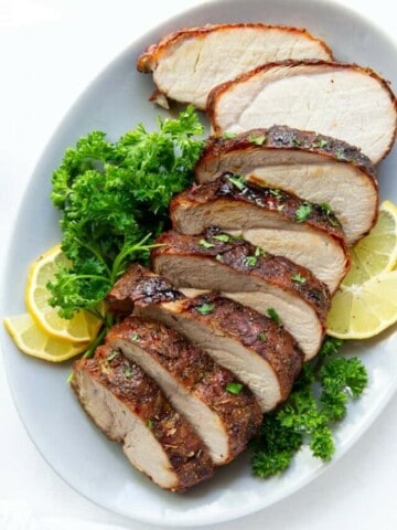 Air Fryer Pork Loin sliced on a plate with parsley and lemons