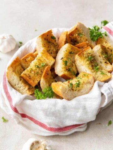 Air Fryer Garlic Bread slices inside a basket with garlic bulbs around it