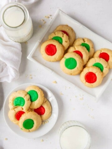 Overhead shot of 2 plates of cookies and glasses of milk on a white background