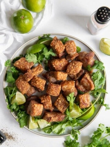 Air Fryer Pork Belly Bites on a plate covered in green garnishes and limes