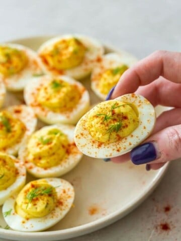 hand grabbing a vinegar-free deviled egg from plate