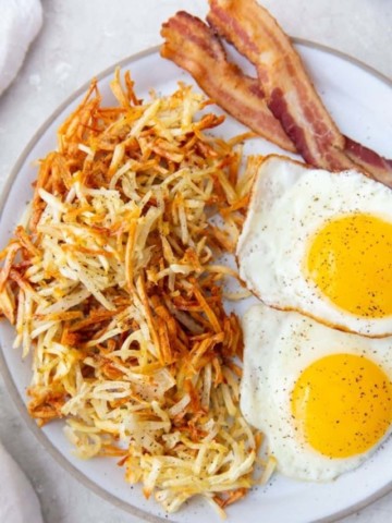 air fryer hash browns on plate with bacon and fried eggs