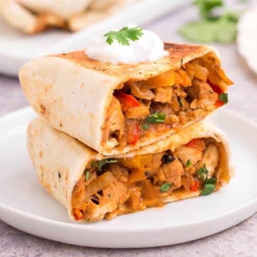 Chicken Fajita Wrap cut in half stacked on a white plate with a dollop of sour cream on top