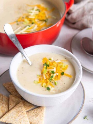 potato soup in white bowl with spoon and toppings sprinkled on