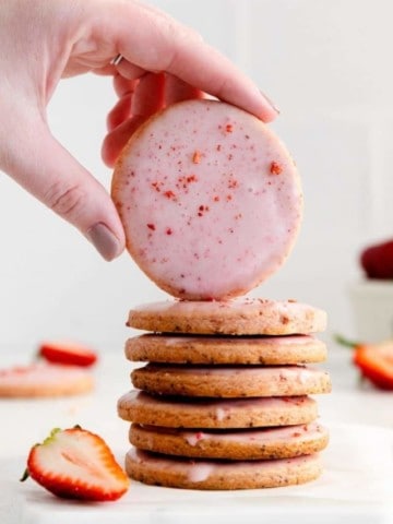 Stack of strawberry shortbread cookies with a hand displaying the top cookie