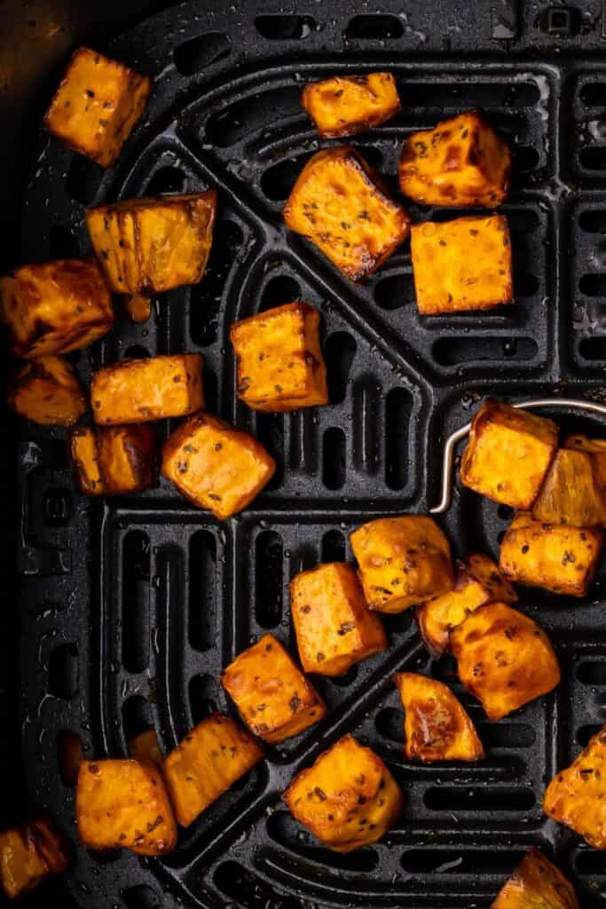 cooked sweet potato cubes in an air fryer basket.