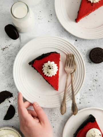 Slice of cheesecake on a plate with a hand grabbing it