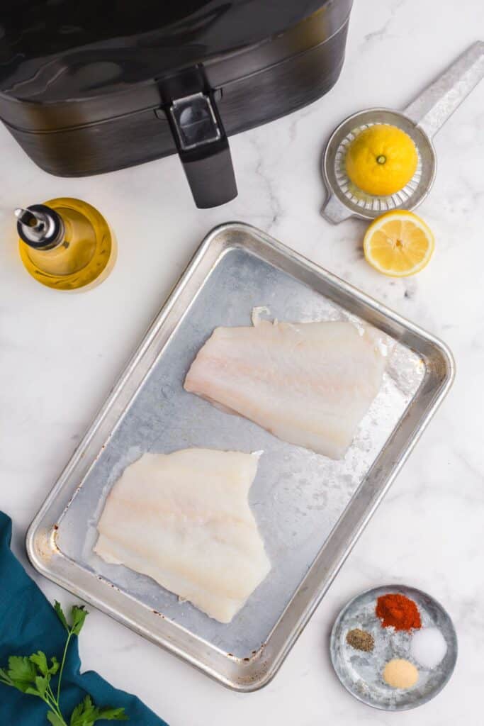 Raw cod with other ingredients needed for the recipe next to an air fryer.