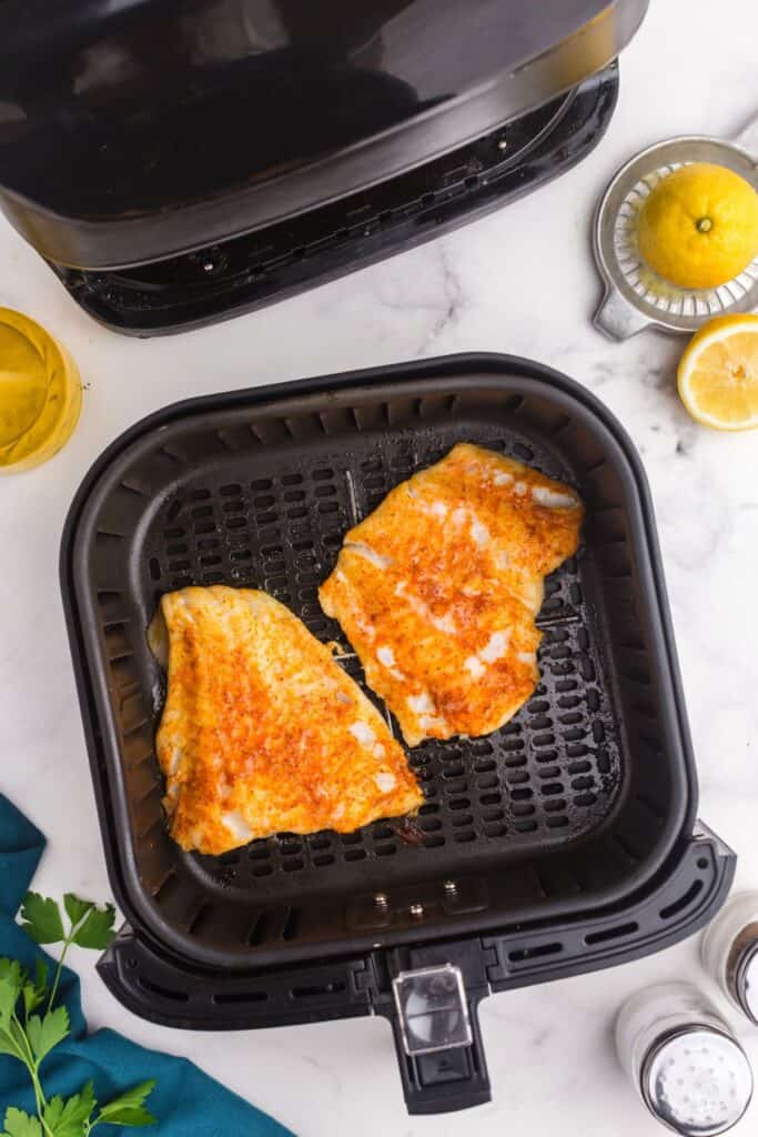 Cooked cod in an air fryer basket.