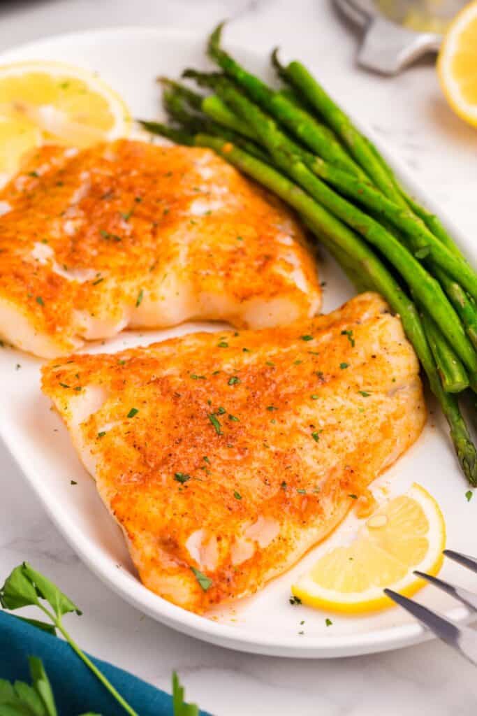 Air fryer cod cooked on a white plate with green beans and lemon