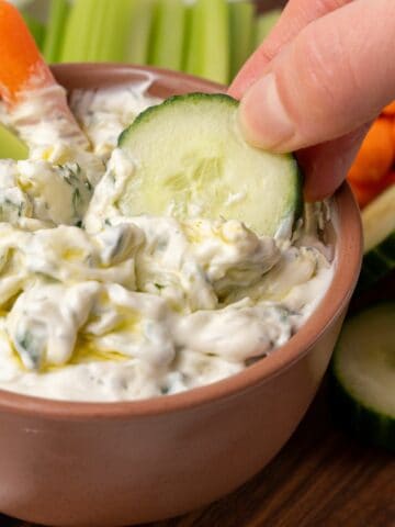 dipping cucumber in Tzatziki Sauce