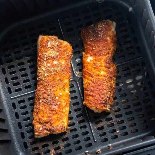 Cooked cod in a black air fryer basket.