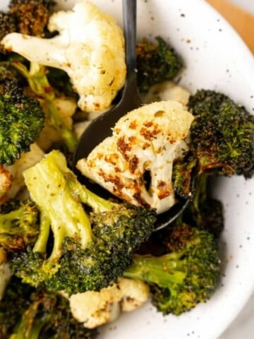 Closeup view of air fried broccoli and cauliflower in a white bowl.