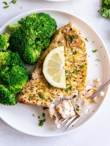 Air Fryer Swordfish on a white plate topped with lemon, served with broccoli.