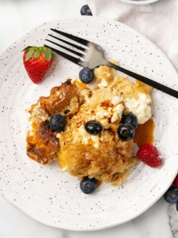 Overhead view of Crockpot French Toast Casserole on a white plate with berries and a fork.