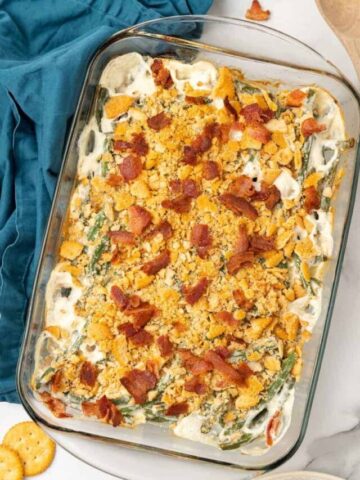 Baked Green Bean Casserole in a clear 9x13 baking dish with crushed bacon sprinkled on top.