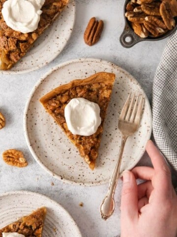 Slices of pecan pie without corn syrup topped with whipped cream on off white plates.