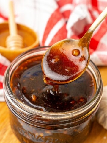 A spoon lifting a small amount of Honey Garlic Sauce out of a small clear mason jar.