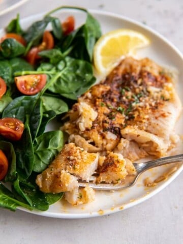 Flounder on a white plate with a salad and lemon wedge.