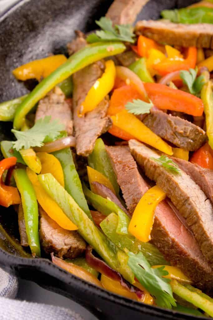 Sliced steak with peppers and onions in a skillet to make steak fajitas.