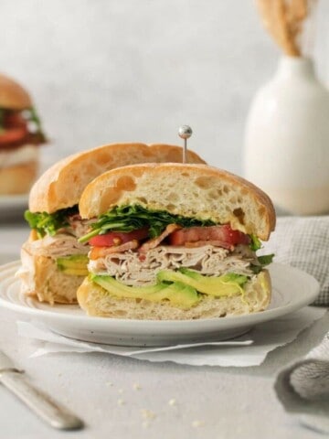 A turkey bacon avocado sandwich sliced in half on a white plate.